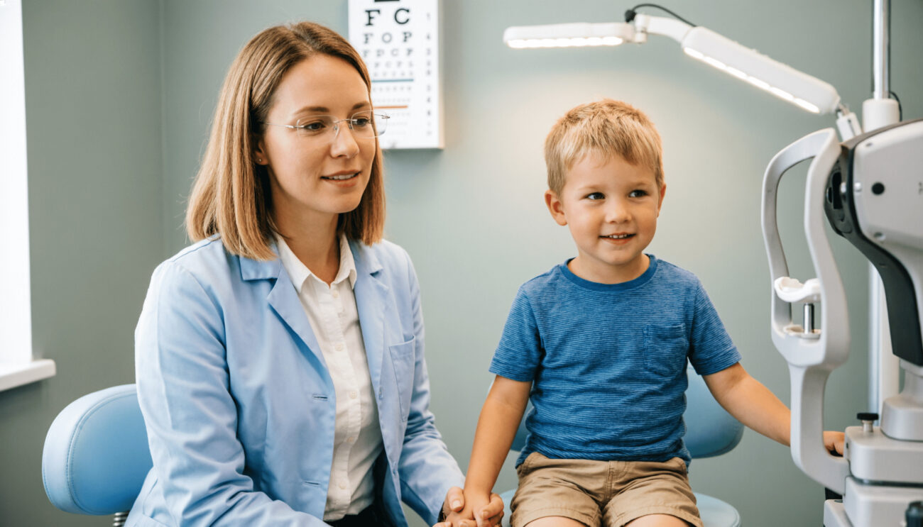 Заботливый детский врач-офтальмолог проводит осмотр ребенка на приеме по лечению халязиона; мама поддерживает малыша в современном медицинском кабинете.